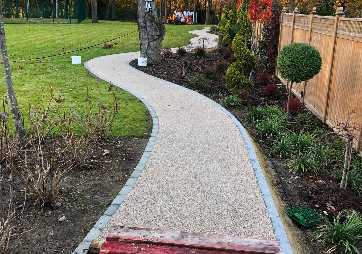 A curved resin-bound garden path in golden aggregate running between planted borders
