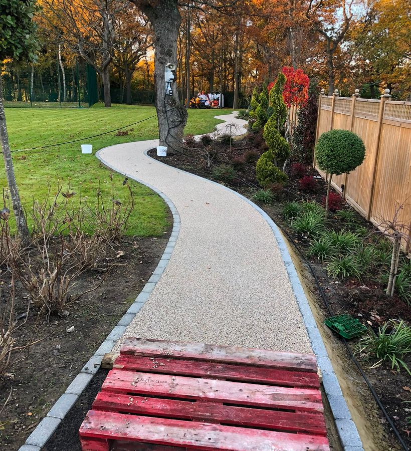 A curved resin-bound garden path in golden aggregate between planted borders